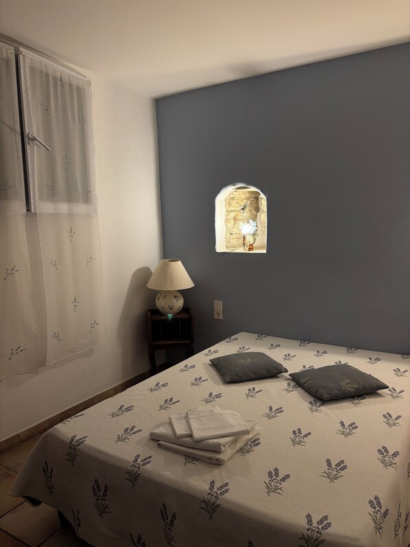 Un dormitorio con cama, mesita de noche, lámpara y ventana con vistas a un muro de piedra.