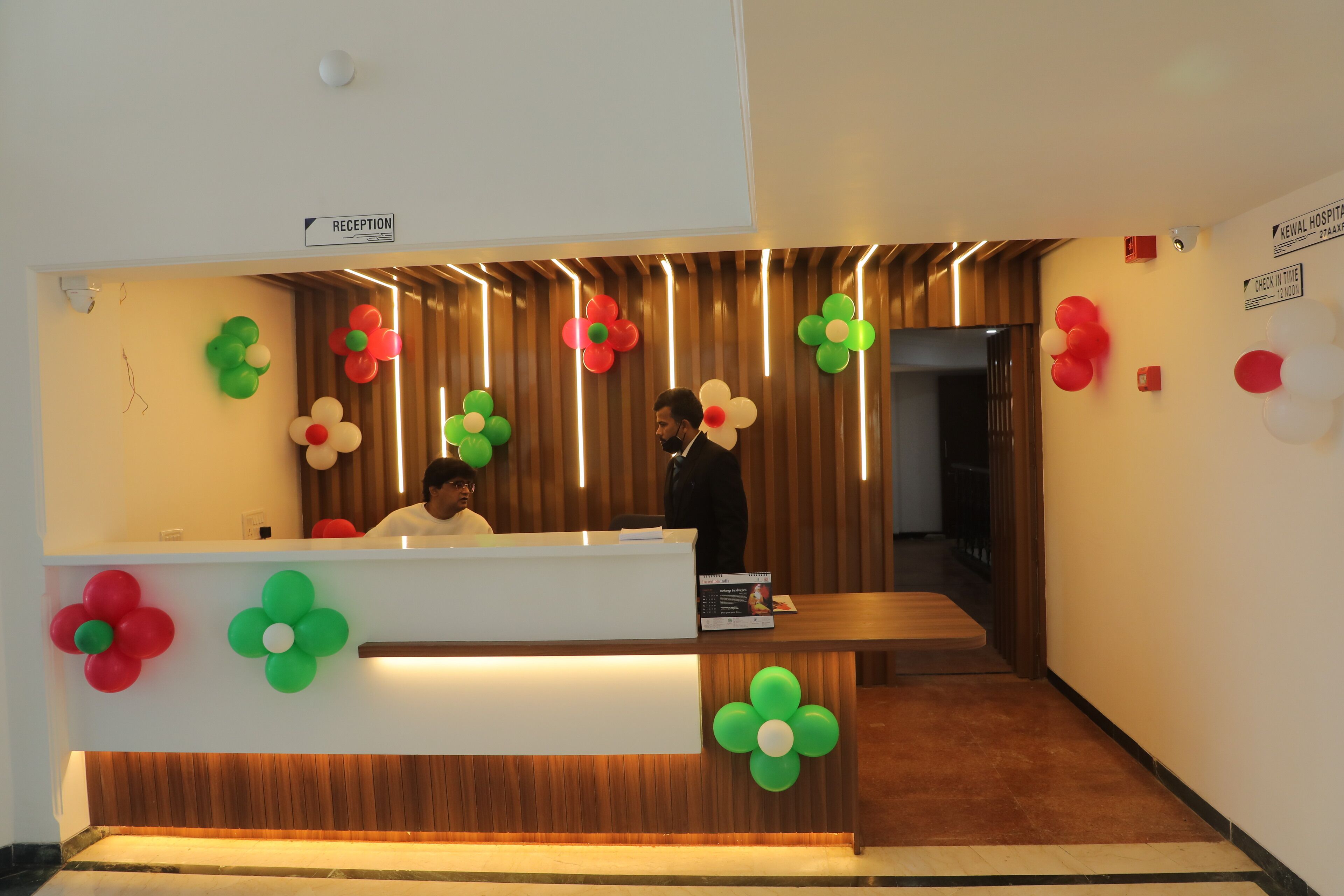 A reception area with a wooden reception desk, a sign indicating the reception, and colorful balloon decorations.