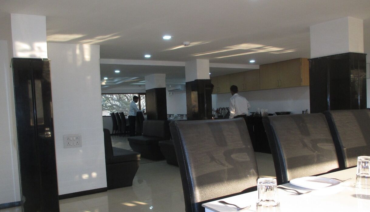 A modern dining area with high-backed chairs, a long table, and a kitchen in the background.