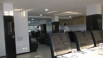 A modern dining area with high-backed chairs, a long table, and a kitchen in the background.