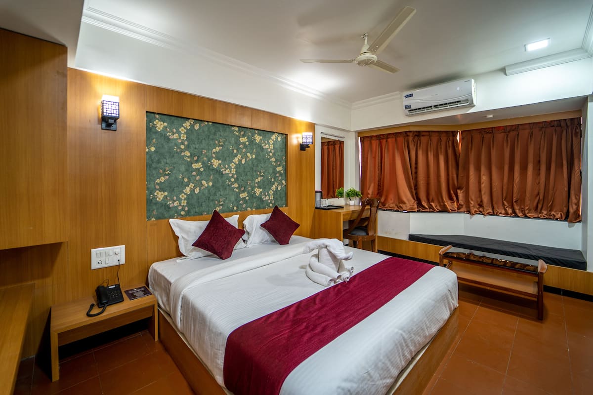 Una habitación de hotel con cama, mesita de noche, lámpara y aire acondicionado.