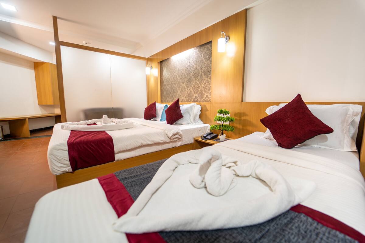 Habitación de hotel con dos camas, cada una con ropa de cama blanca y detalles en rojo, una mesita de noche con una planta y un cabecero de madera.