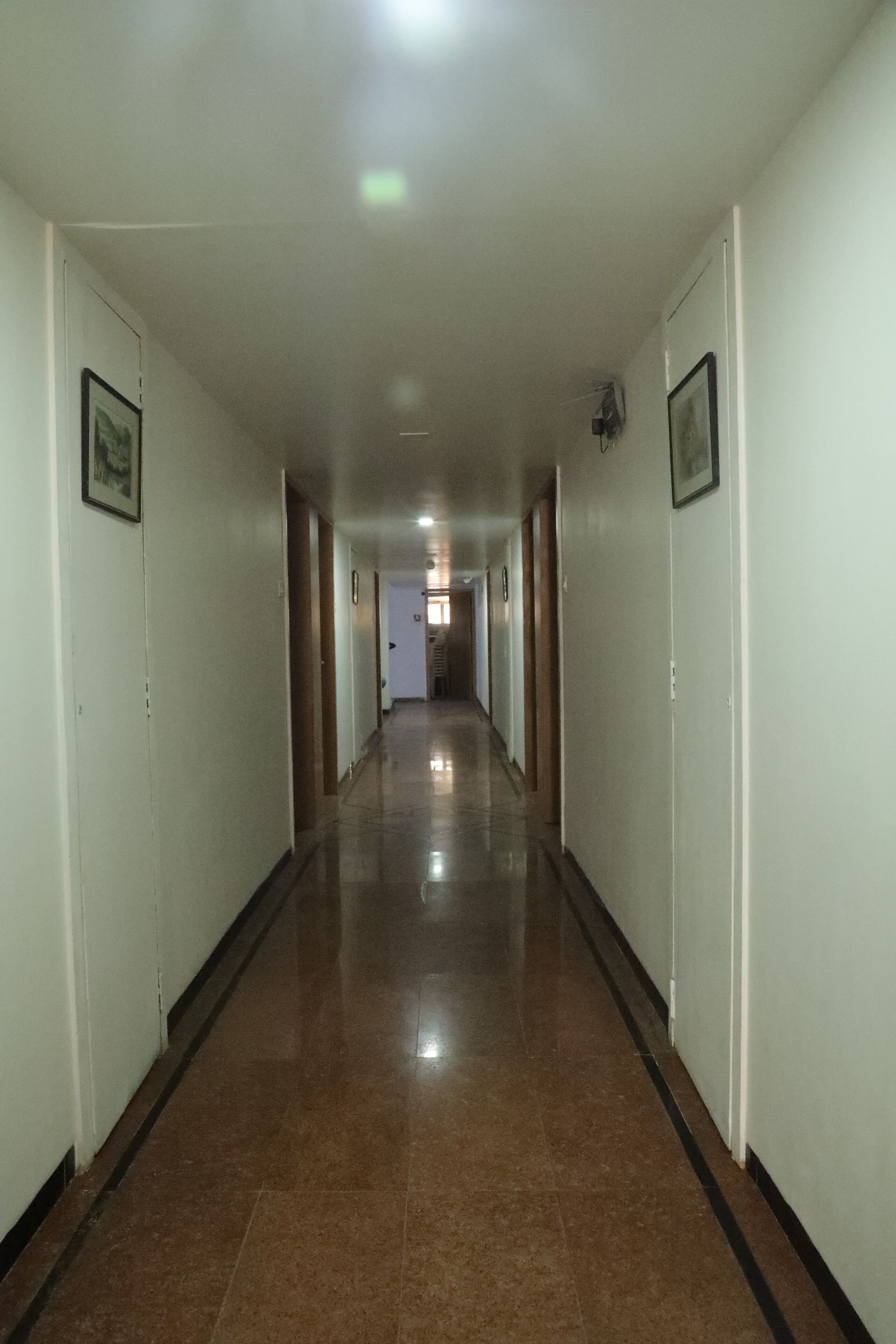 A long, narrow hallway with white walls and a shiny brown floor.