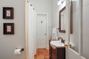 A bathroom with a white door, a sink with a mirror, and framed pictures on the wall.