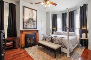 A four-poster bed with a bench, a fireplace, and a ceiling fan.