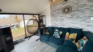 A modern living room with a teal sofa, a round hanging chair, and a stone-patterned wall.