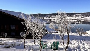 A snow-covered outdoor area with picnic tables and benches, a building in the background, and a clear blue sky.