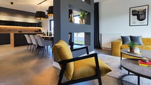 A modern living room with a sofa, a dining area with chairs, and a kitchen in the background. - Stylish Designer Villa with Pool & Guest Apartment Near the Sea (Nedescina)