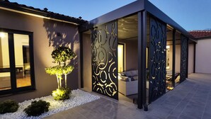 A modern house with a patio, a decorative wall, and a well-lit garden. - Stylish Designer Villa with Pool & Guest Apartment Near the Sea (Nedescina)