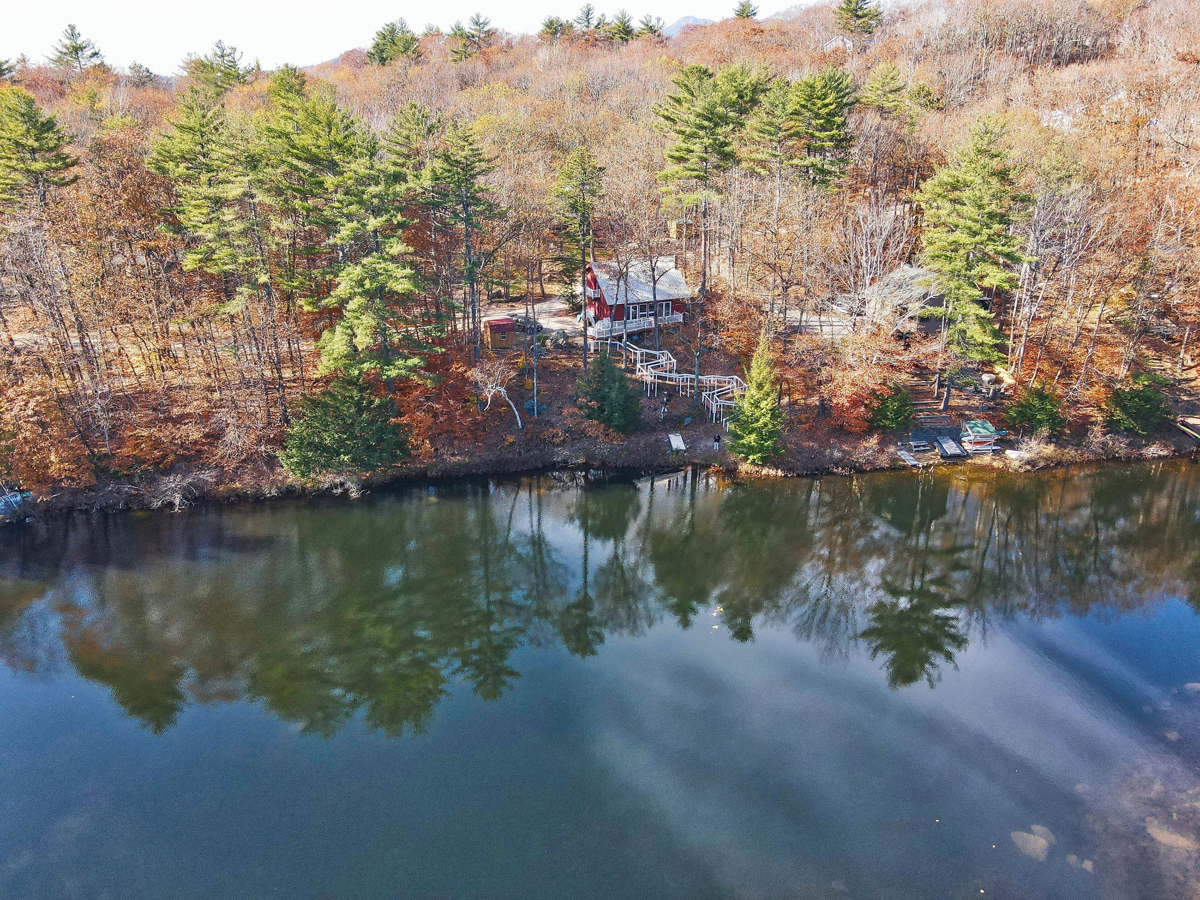 Una cabaña con un muelle que se adentra en un lago tranquilo, rodeada de un bosque denso con follaje otoñal.