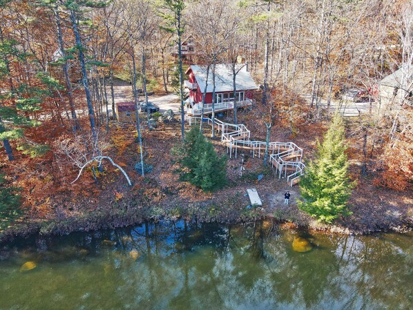 A cabin with a deck and a dock extending into a lake, surrounded by trees and autumn foliage.