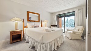 A spacious bedroom with a large bed, two bedside tables, a chair, and a view of snow-covered trees through a large window. - Rock Pond Condo 45 - Beautiful Ski in/Ski out condo unit on Saddleback! (Rangeley)