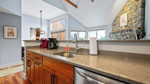A kitchen with wooden cabinets, a stainless steel dishwasher, a granite countertop, and a stone wall. - Rock Pond Condo 45 - Beautiful Ski in/Ski out condo unit on Saddleback! (Rangeley)