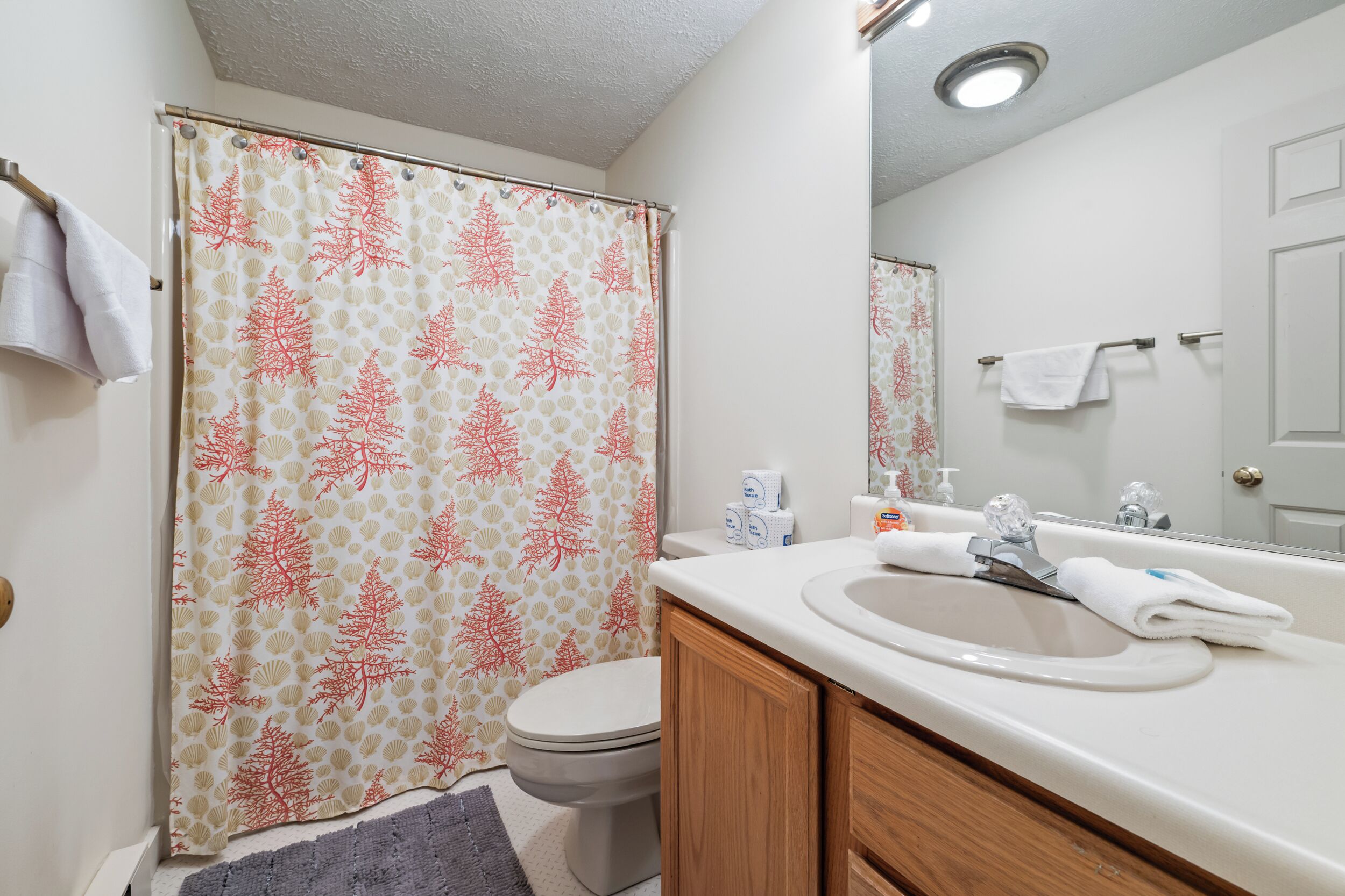 A bathroom with a shower curtain, toilet, sink, and mirror.