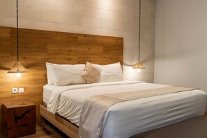 Een slaapkamer met een houten hoofdeinde, wit beddengoed en twee hanglampen.