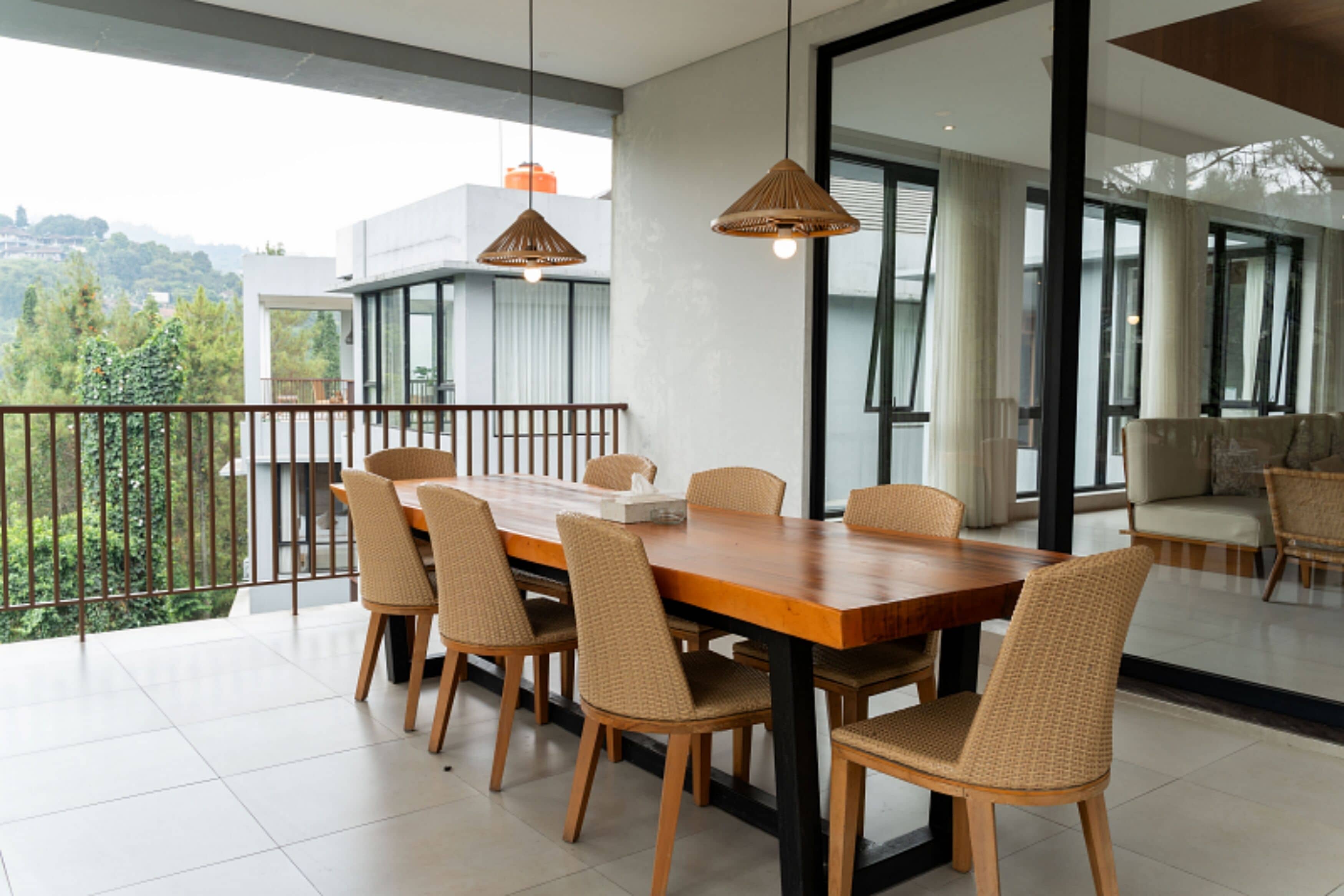Un comedor con mesa de madera, sillas de mimbre, ventanas amplias y vistas a zonas verdes.