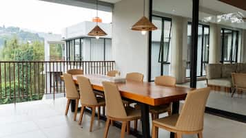 Un comedor con mesa de madera, sillas de mimbre, ventanas amplias y vistas a zonas verdes.