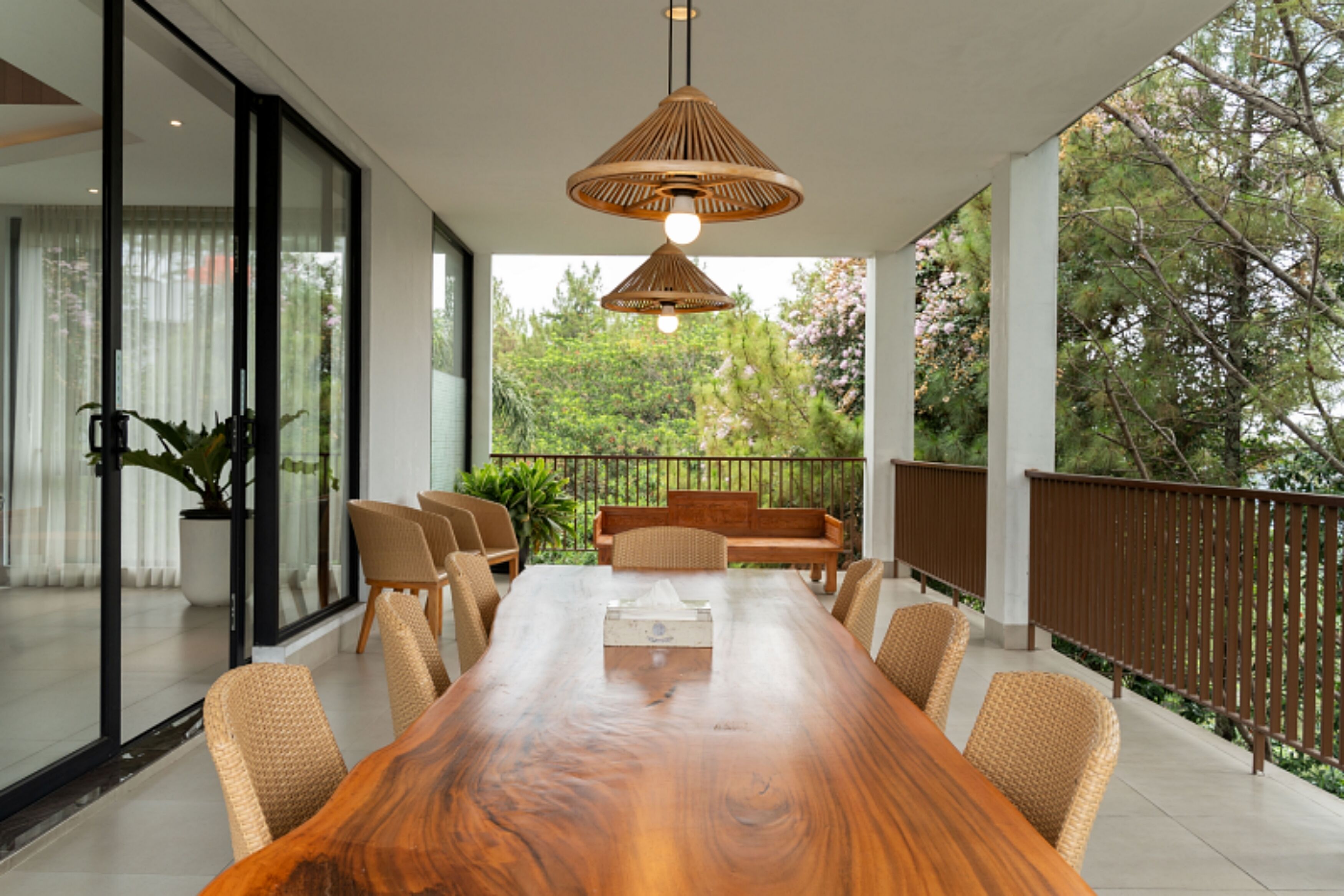 Un comedor moderno con una larga mesa de madera, sillas de mimbre y un colgador de luz.