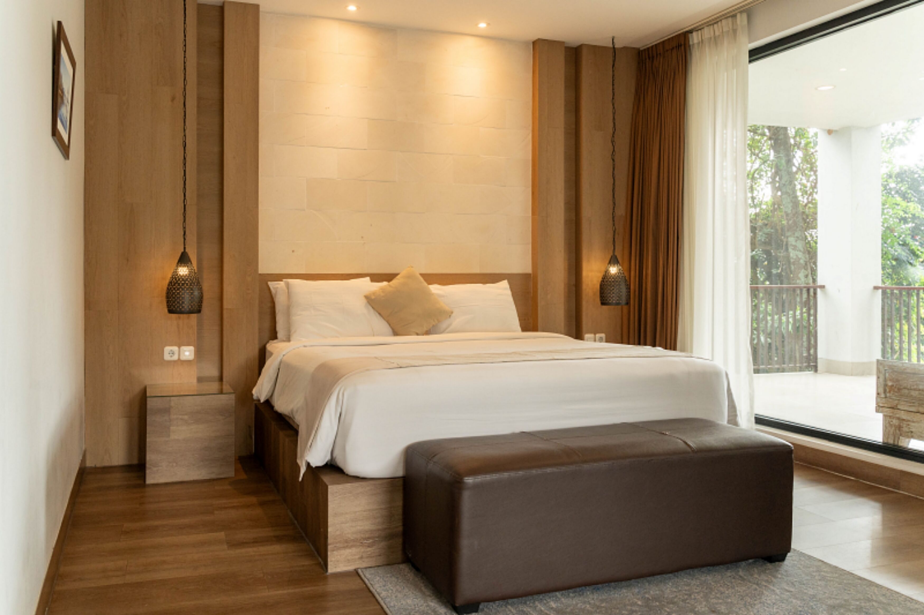Ein modernes Schlafzimmer mit einem großen Bett, einer hölzernen Bank und Blick ins Freie.