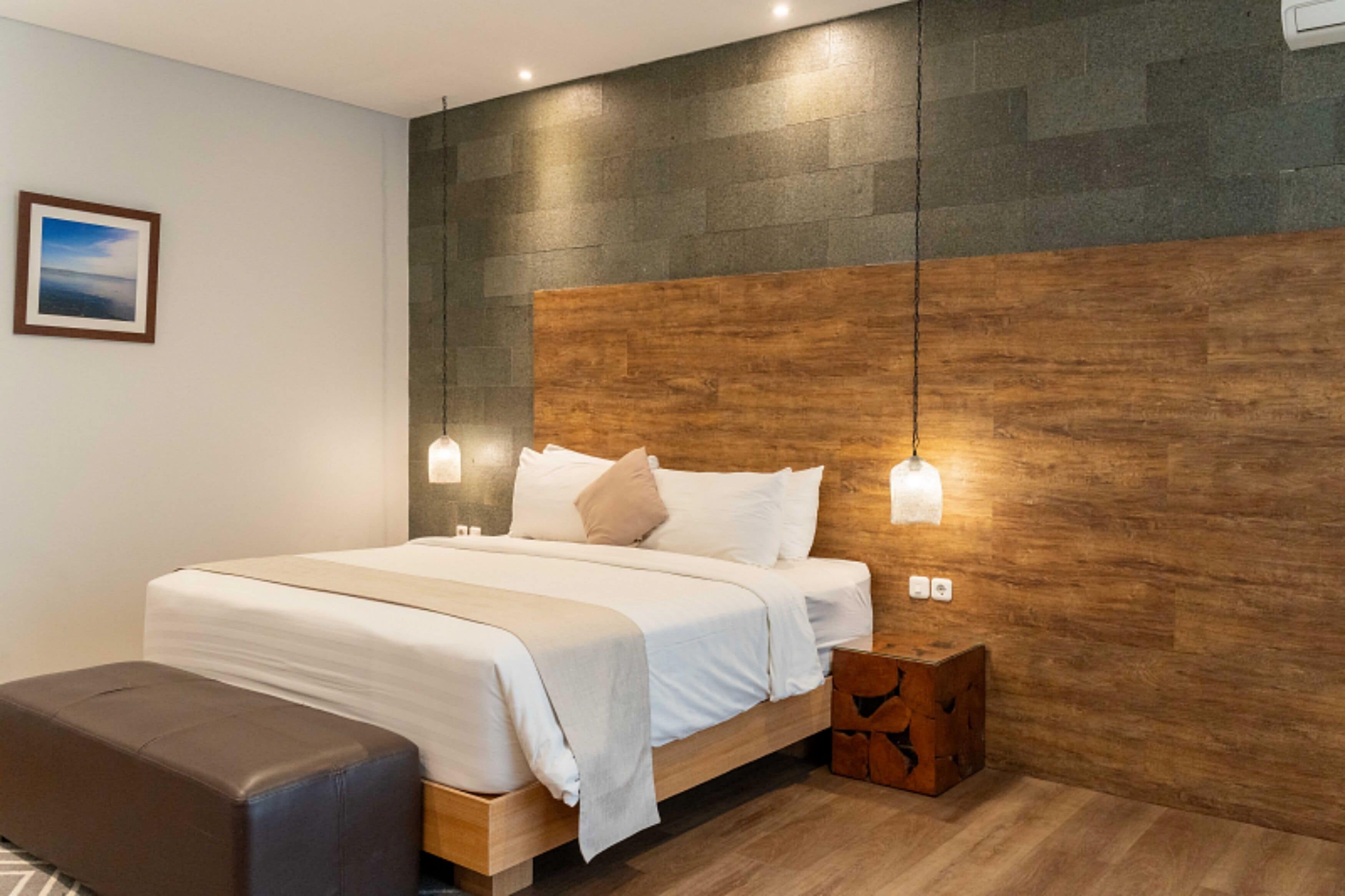 Una habitación de hotel moderna con cabecera de madera, cama con ropa de cama blanca, una mesita de noche y un banco.