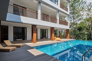 A modern two-story building with a swimming pool, outdoor seating, and a balcony with wooden railings.