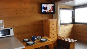 A cozy cabin interior with a wooden table set for dining, a microwave, a television mounted on the wall, and a window providing natural light. - 200m from ski slopes, 4th floor, tv, 31m², Val Thorens (Val Thorens)