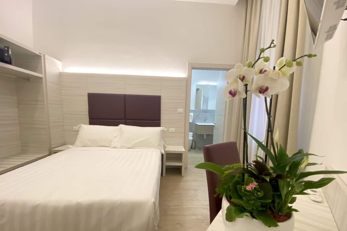 Una habitación de hotel con cama, mesita de noche, silla y una planta en maceta.
