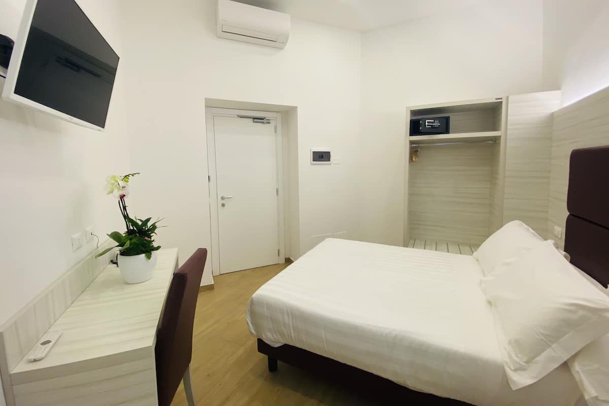 Habitación de hotel con cama, escritorio, silla, planta en maceta, televisor, aire acondicionado y armario.