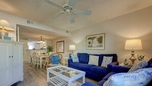 Ein Wohnzimmer mit einem blauen Sofa, einem weißen Couchtisch und einem Deckenventilator.