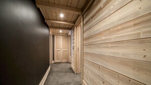 Un couloir étroit aux murs en bois et au sol en béton, qui mène à une porte au fond.