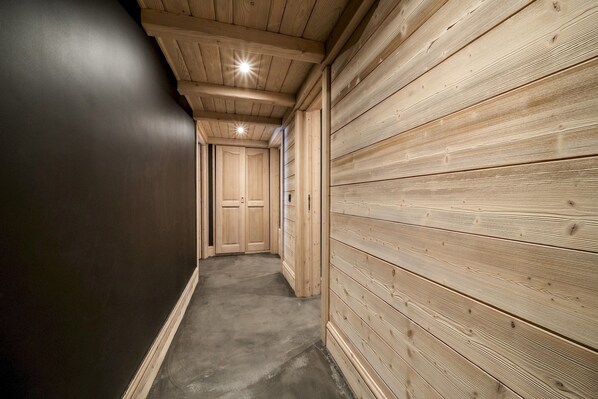 A narrow hallway with wooden walls and a concrete floor, leading to a door at the end.