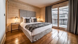 Une chambre aux murs lambrissés, dotée d’un grand lit, de deux tables de chevet avec des lampes et d’un balcon agrémenté de rideaux.