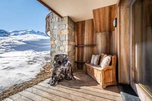 A wooden deck with a stone wall, a bench, and a view of a snowy mountain landscape.