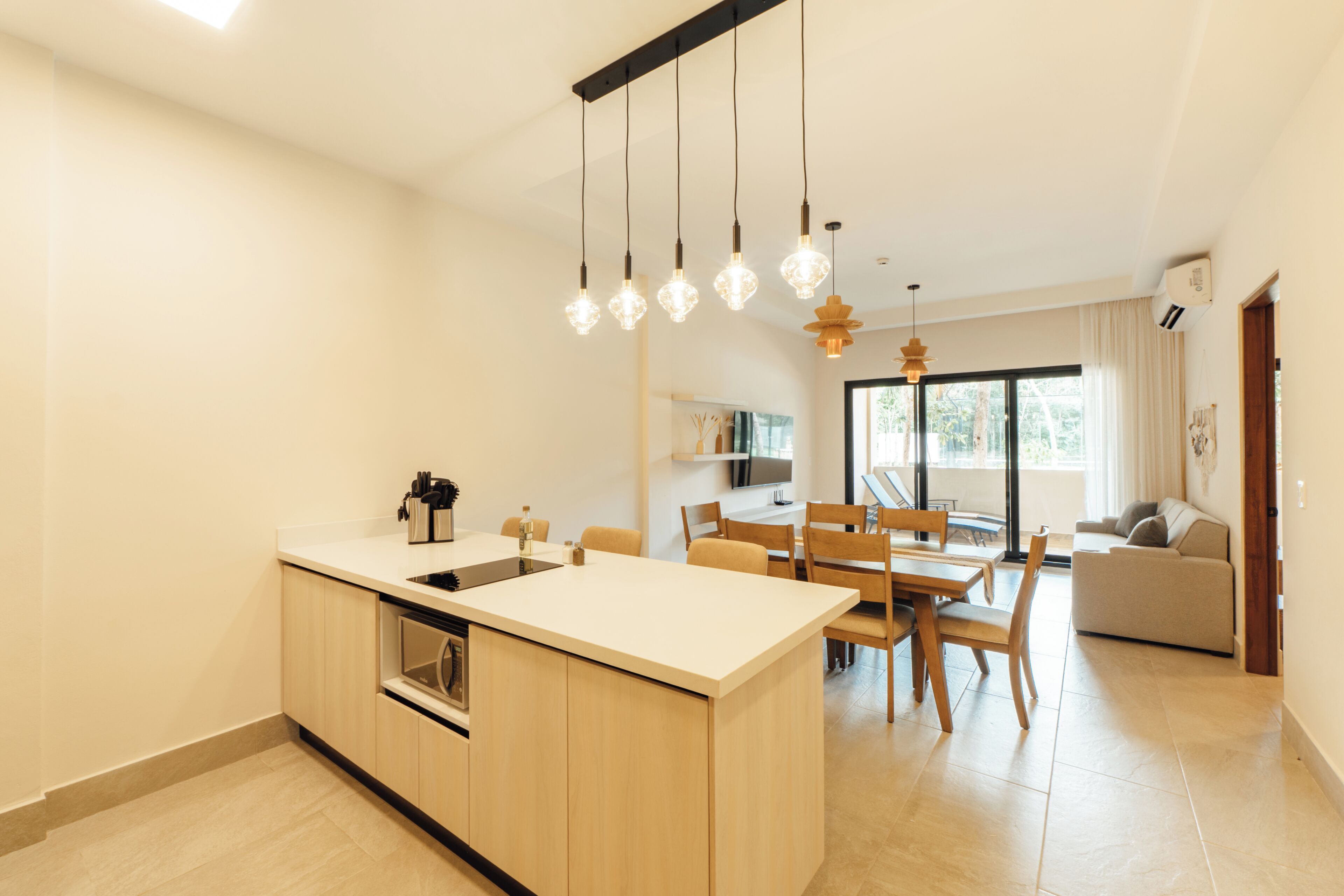 A modern kitchen with a central island, dining area with chairs, and a sofa in a bright living space.