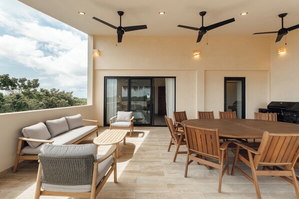 A spacious outdoor patio with a wooden dining table, chairs, a sofa, and ceiling fans.
