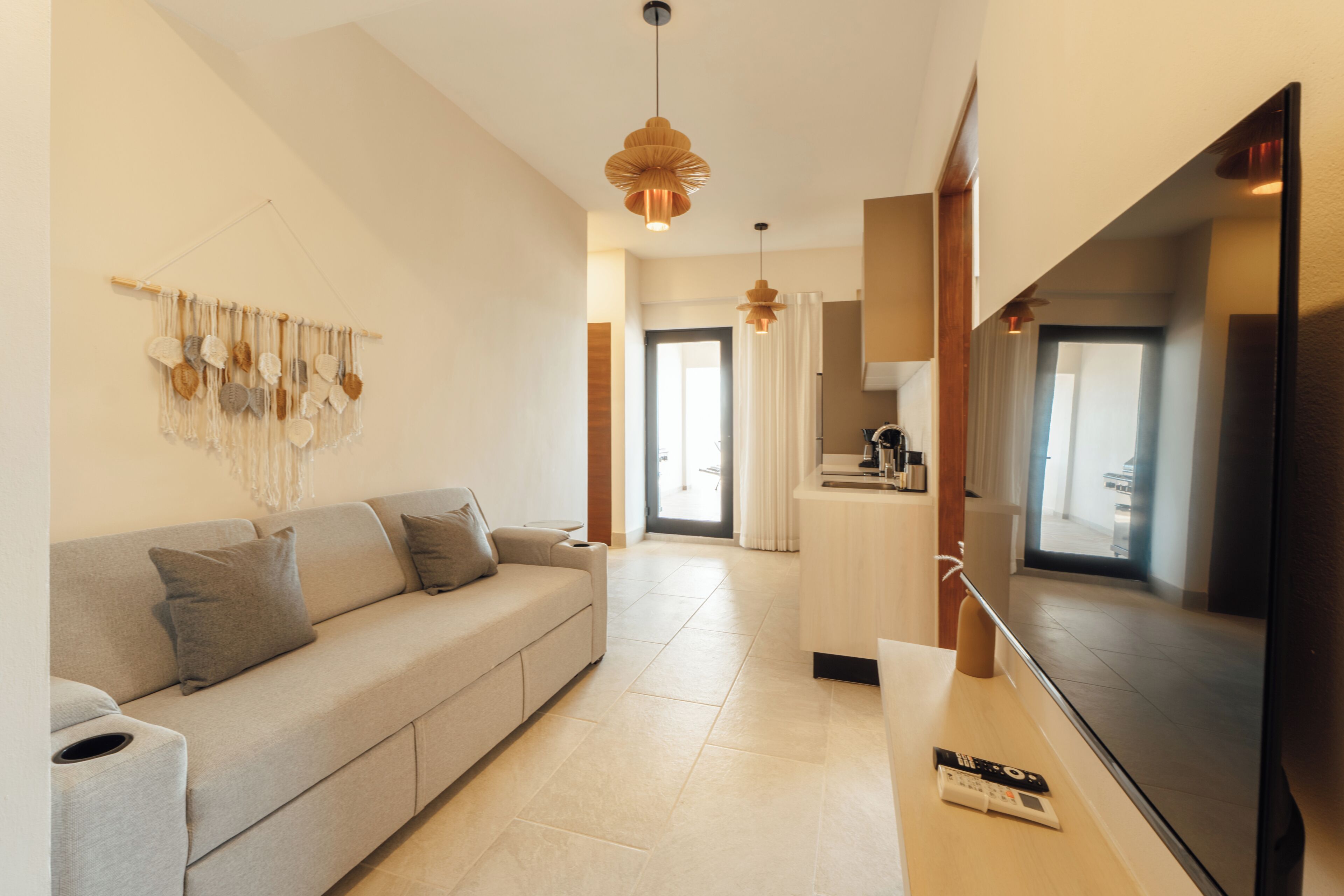 Una sala de estar moderna con sofá, televisión y una cocina al fondo.