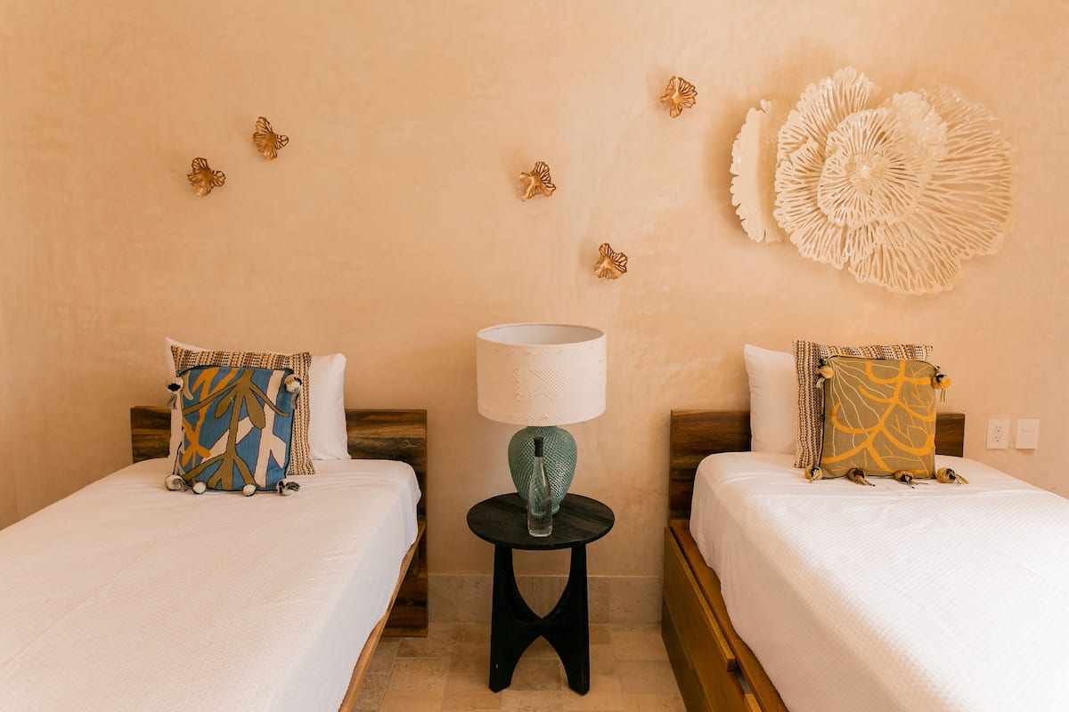Une chambre d’hôtel avec deux lits, une table ronde avec une lampe et des œuvres d’art décoratives au mur.