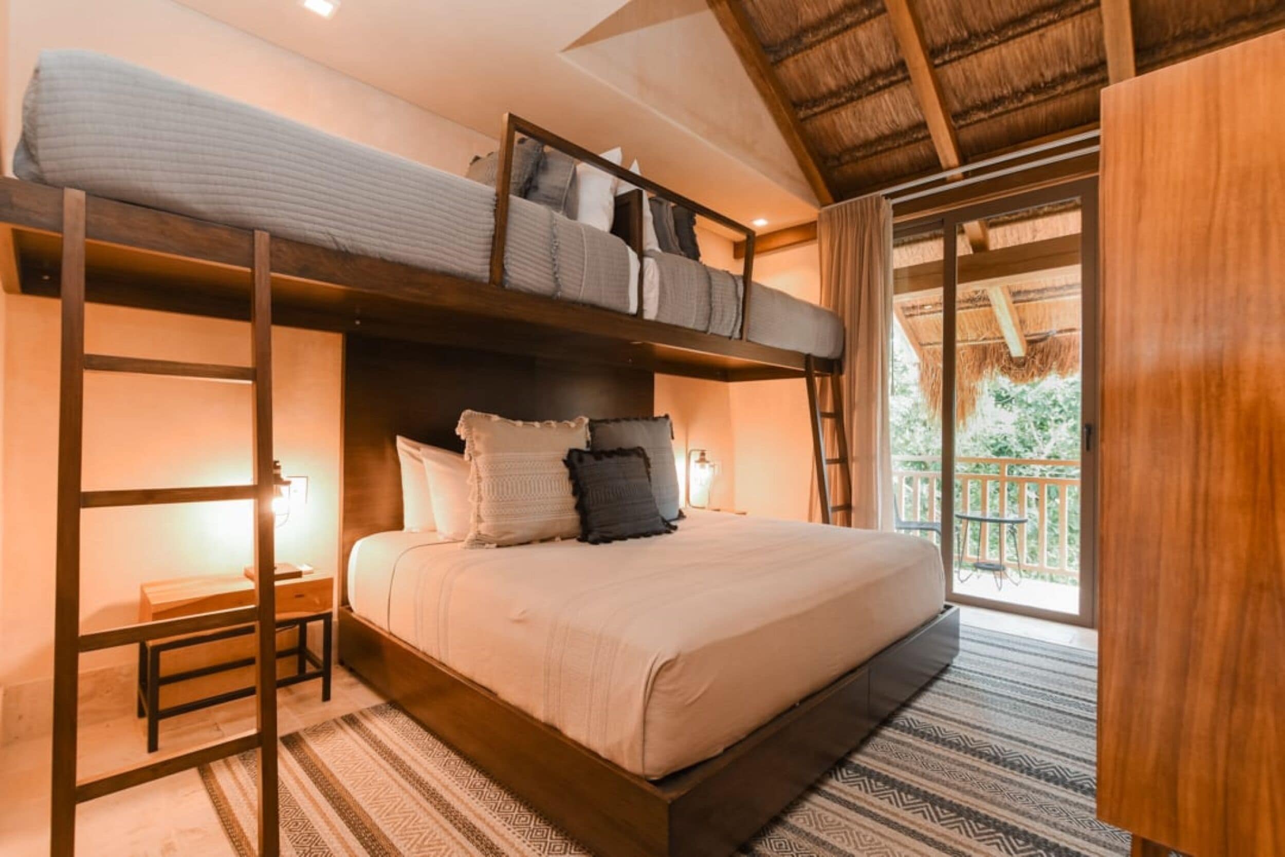 A bunk bed room with a wooden ladder, a bedside table, and a view of the outdoors.
