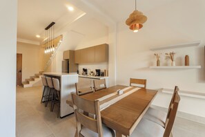 A modern kitchen with a central island, wooden dining table, and bar stools. - Lumina at LOSANTOS Tulum (Tulum)