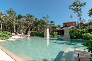 A clear swimming pool surrounded by lush greenery and a wooden structure. - Lumina at LOSANTOS Tulum (Tulum)