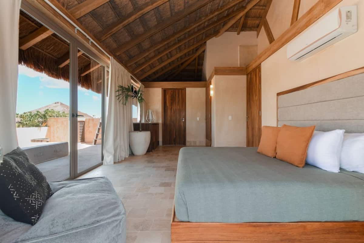 Une chambre dotée d’un grand lit, d’un canapé et d’une porte-fenêtre coulissante donnant sur un espace extérieur.