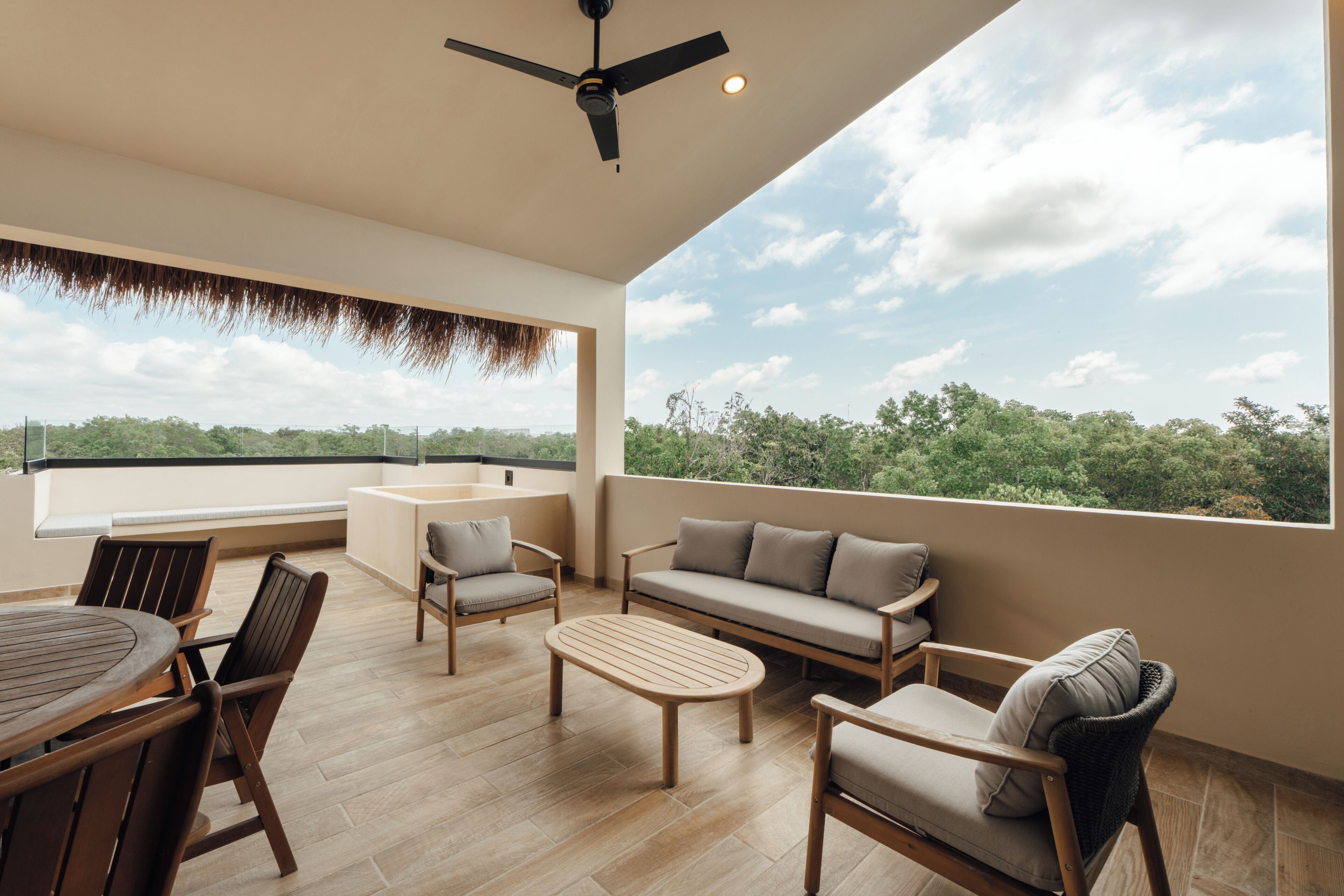 A spacious balcony with a wooden table, chairs, a sofa, and a ceiling fan.