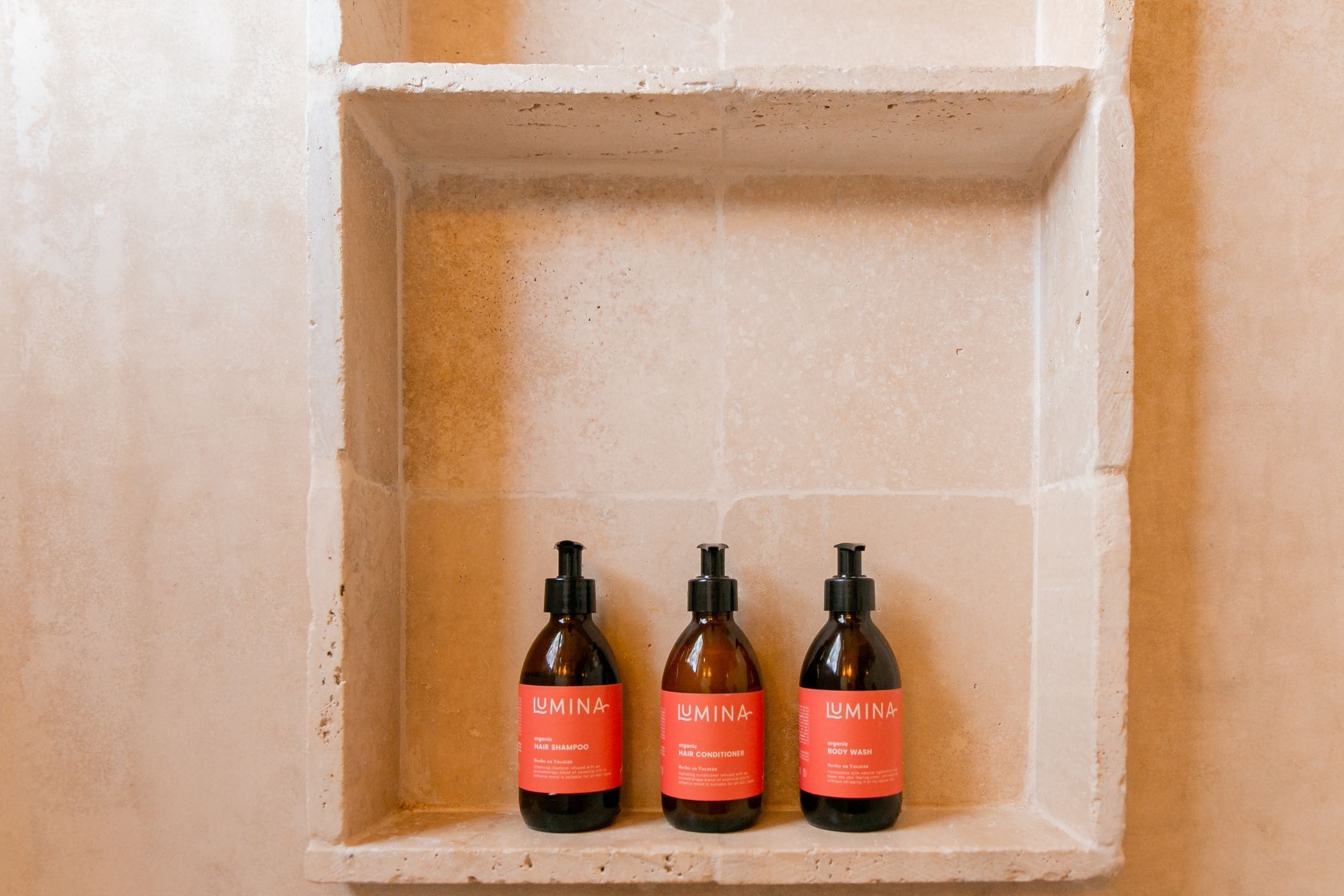 Three bottles of Lumina products in a shelf against a textured wall.