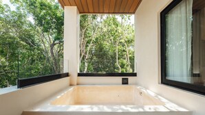 A modern bathroom with a large bathtub, a window with a black frame, and a view of trees. - Lumina at LOSANTOS Tulum (Tulum)