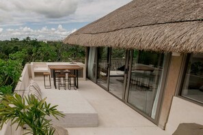 A modern outdoor patio with a thatched roof, a dining table with stools, and a glass-enclosed area.