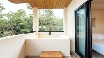 A modern bathroom with a bathtub, a wooden bench, and a large window offering a view of trees.