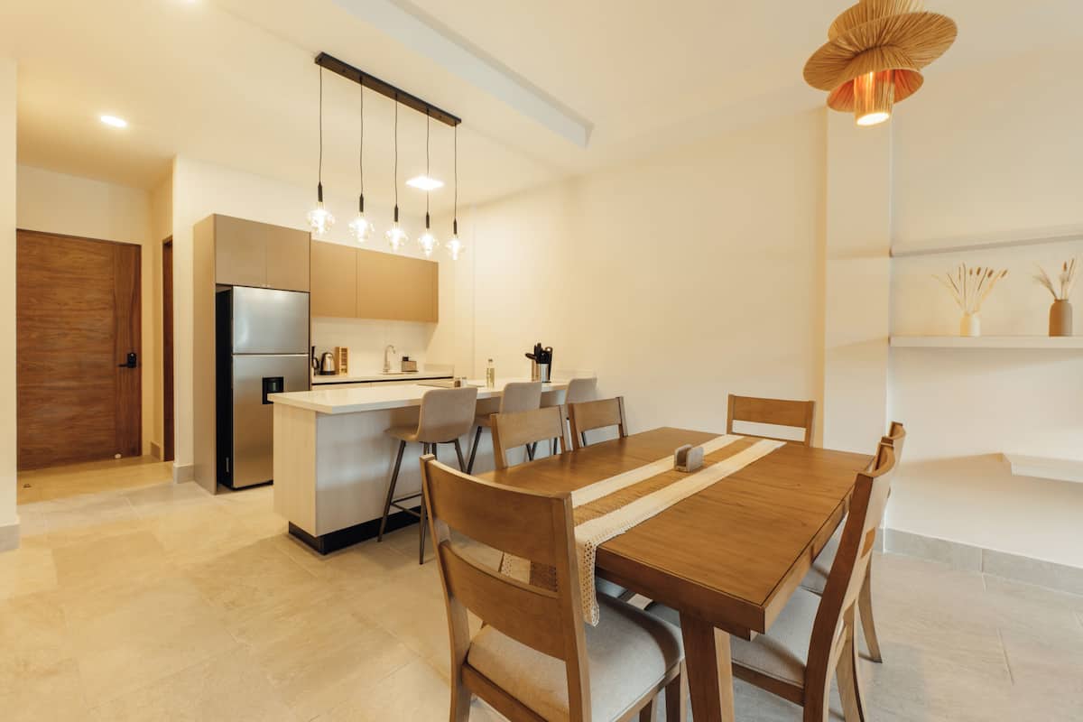 Une cuisine moderne avec un coin repas, des chaises en bois, un îlot central et des luminaires suspendus.