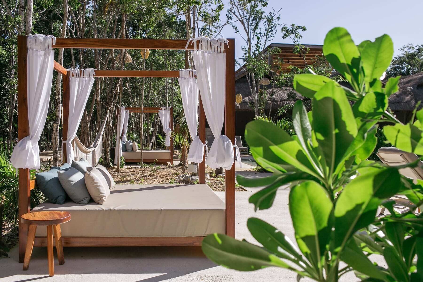 A wooden bed with a canopy, a small wooden stool, and a hammock in a garden setting.