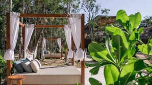 A wooden bed with a canopy, a small wooden stool, and a hammock in a garden setting.