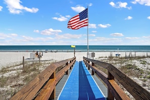 Un paseo marítimo de madera que conduce a una playa con una bandera estadounidense y una bandera de salvavidas.